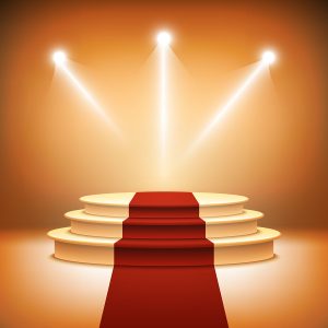 Staircase with red carpet leading to spotlighted stage, symbolizing success and achievement.