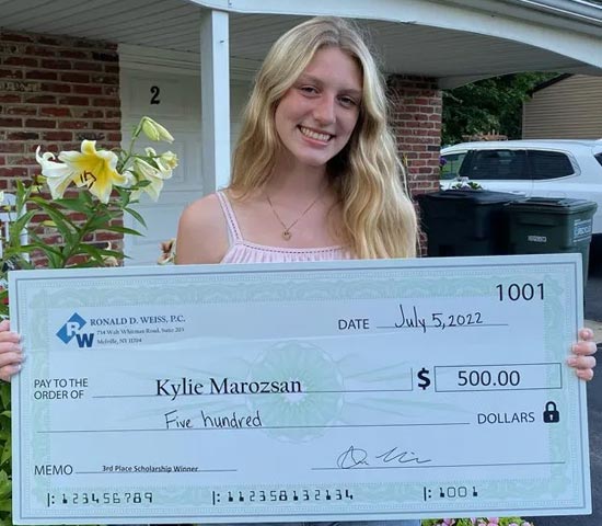 A person holding a large ceremonial check from Associated Women PAs, awarded to Kylie Manossian for $500 as the 'PA Pride Scholarship Winner,' dated July 5, 2021