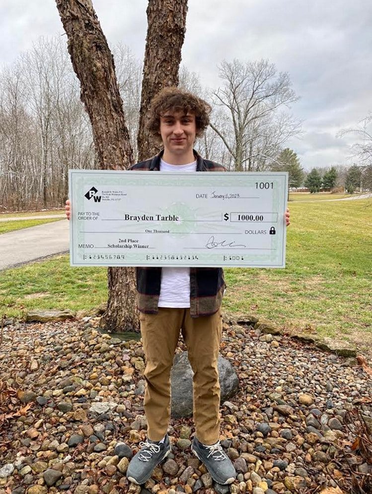 Young man holding oversized scholarship check outdoors.