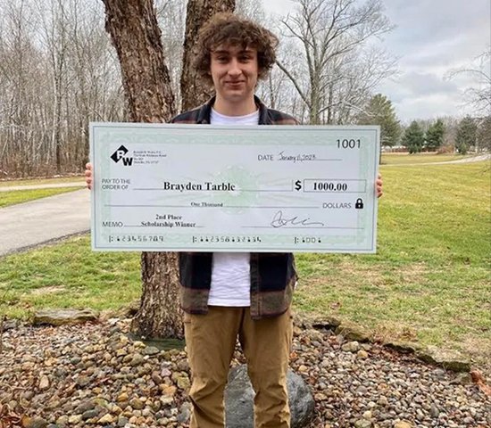 $1000 scholarship check awarded to smiling young man outdoors in park | Long Island bankruptcy and foreclosure law firm.