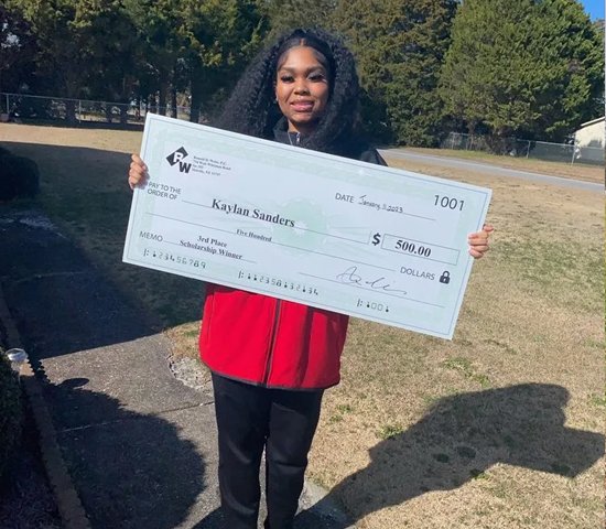 $500 scholarship check awarded to smiling young woman outdoors.
