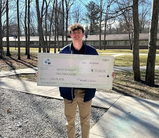 Young man holding a large check outdoors on a sunny day.