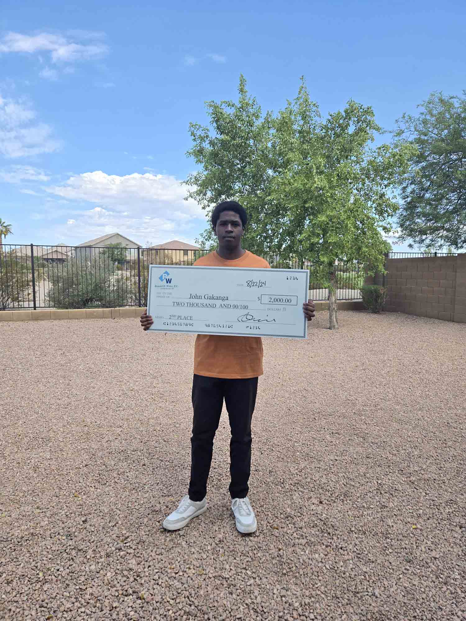 $2,000 prize winner holding a check outdoors on a sunny day.