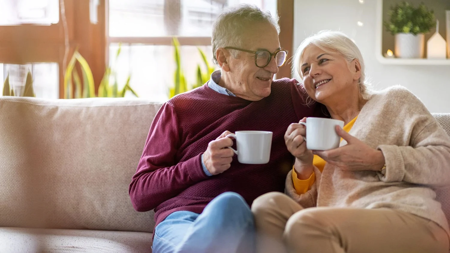 An older couple smiling and sharing coffee at home